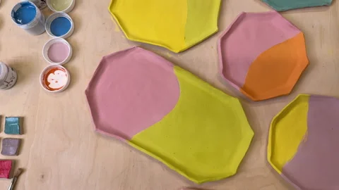 Top view of handmade clay plates covered with colored glazes and glaze jars, rea Stock Footage 306278410