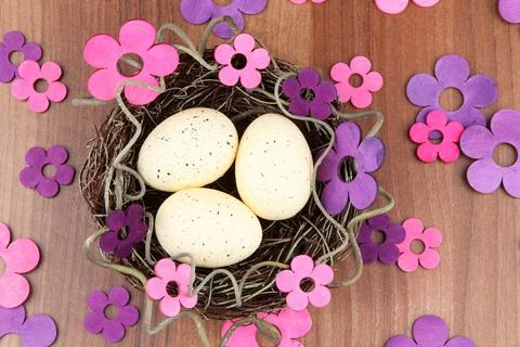 Top view of handmade Easter nest with eggs and flowers in lilac tones, on a wood 스톡 사진