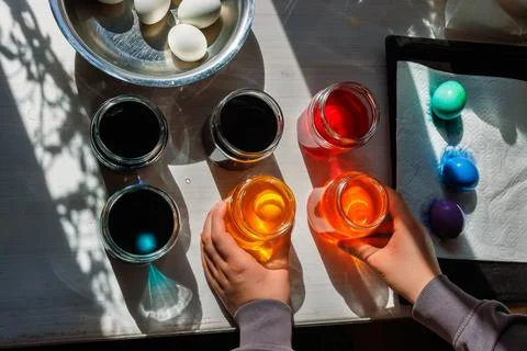 Top view of the hands arranging dye jars for easter egg coloring on sunlit .. Stock Photos