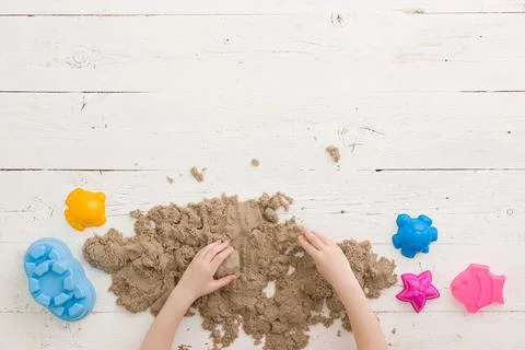Top view on the hands of a child playing with kinetic sand and tins on a table Stock Photos