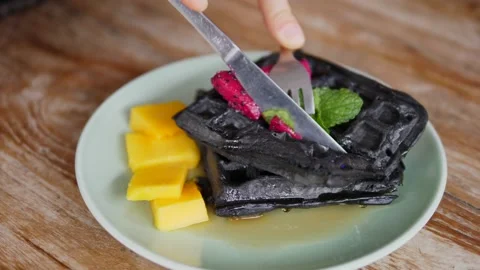 Top view of hands cutting black Belgian vegan waffles with silver cutlery Stock Footage 146784202