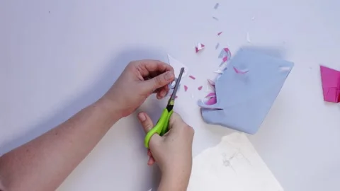 Top view of hands cutting colored paper with scissors, scraps scattered on white Stock Footage 316470891