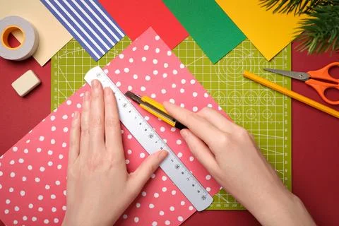 Top view of hands cutting patterned paper with craft knife and ruler on cut.. Stock Photos