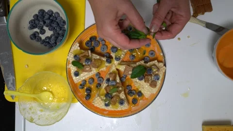 A top view of hands decorating a dessert with blueberries, mint leaves, and a Stock Footage 336062256