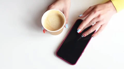 Top view hands holding coffe cup and pressing smartphone on white background. Co Stock Footage 242492644