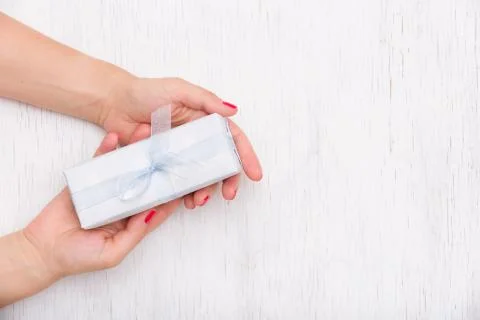 Top view on hands holding gift box with ribbon on white wooden background Stock Photos