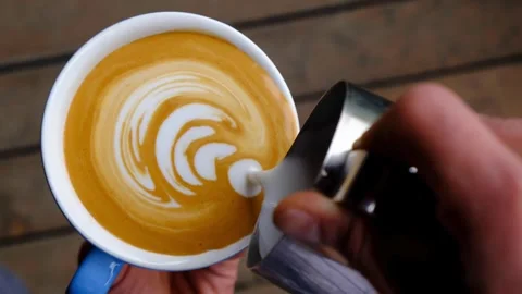 Top view of hands making art on latte coffee by pouring milk on a cup of coffee. 動画素材 334647926