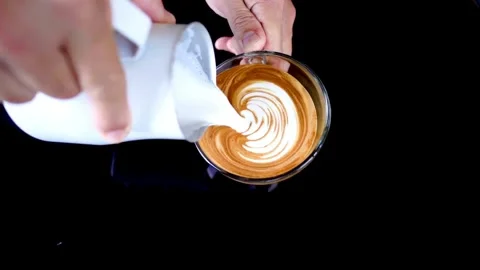 Top view of hands making art on latte coffee by pouring milk on a cup of coffee. 動画素材 334648006