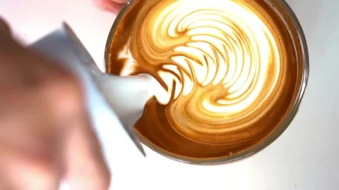 Top view of hands making art on latte coffee by pouring milk on a cup of coffee. 動画素材 334648048