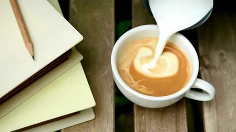 Top view of hands making art on latte coffee by pouring milk on a cup of coffee. Stock-Footage 334648556
