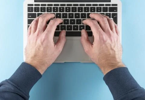 Top view of hands of man typing on laptop computer on blue desk background Stock Photos