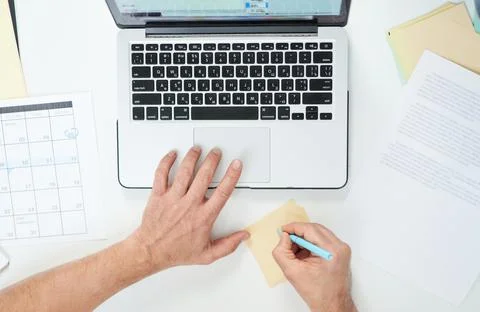 Top view of hands of man working with his laptop and writing sticky notes on the Stock Photos