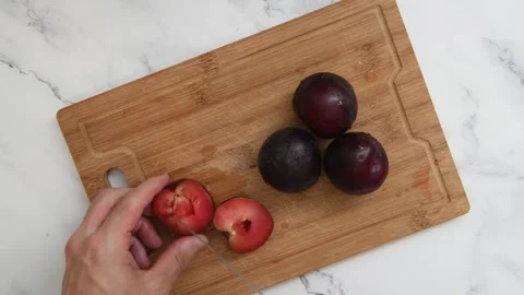 Top view of hands removing pits from fresh plums with a knife on a wooden Stock Footage 325450762