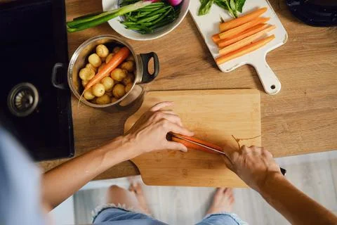 Top view of hands slicing fresh carrot lengthwise on wooden chopping board .. Stock Photos