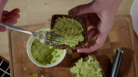 Top view hands spreading avocado on dark bread on wooden cutting board Stock Footage 329930514