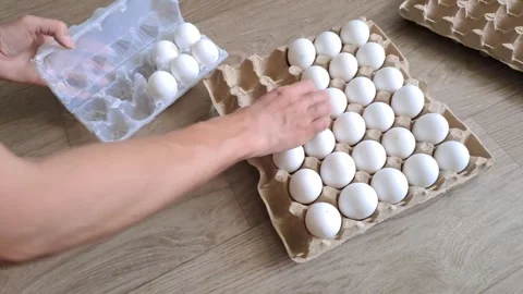 Top view of hands transferring white chicken eggs from a large cardboard crate i Stockbeeldmateriaal 338008312