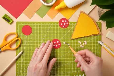 Top view of hands using tweezers to assemble a paper pizza sausage on a green Stock Photos