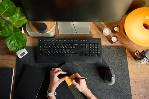 Top view of hands writing on sticky note at desk with monitor, keyboard, mo.. 스톡 사진