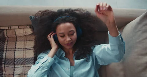 Top view happy beautiful mixed race student woman lies down on couch, listens to Stock Footage 148494890