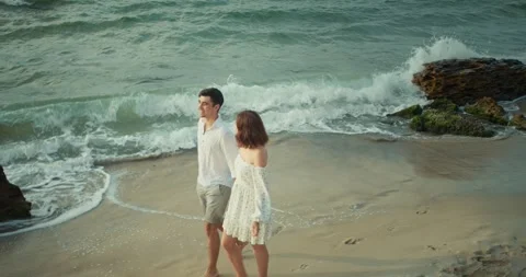 Top view of a happy brunette guy in a white shirt walking along the beach with Stock Footage 283834455