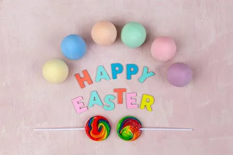 Top view of Happy Easter text with colorful eggs and lollies on textured back Stock Photos