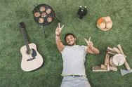 Top View Of Happy Young Man Resting On Grass With Guitar And Food For Picnic Stock Photos