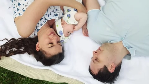 Top view happy young parents kiss infant baby child lying on a rug at park Video stock 344844174
