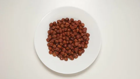 TOP VIEW: Hazelnuts fill a white dish (stop motion) Видео 69809276