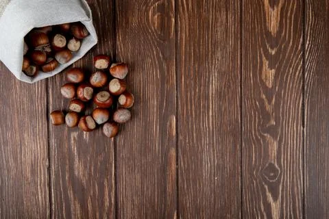 Top view of hazelnuts in shell scattered from a sack on wooden background w.. Stock Photos