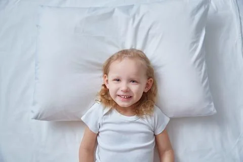 Top view head curly-haired girl's child lying bed white sheet, pillow. Mockup Stock Photos