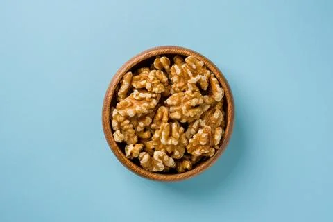 Top view of heap of walnut kernels in wooden bowl on blue background Stock Photos