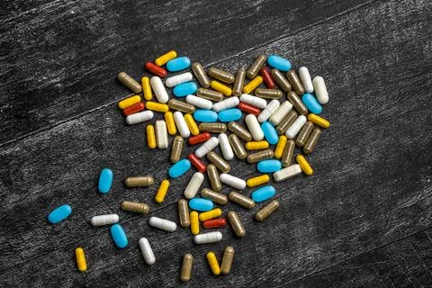 Top view of heart of multi-colored medical capsules and pills on a black back Stock Photos