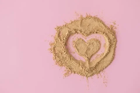 Top view of heart shape made of raw maca root powder on soft pink background Фото