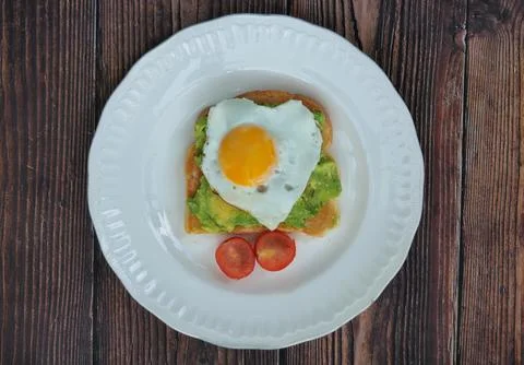 Top view of Heart shaped fried egg on smashed avocado and tomato on a white.. Stock Photos