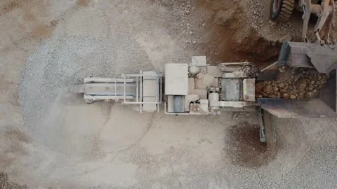 Top view of a heavy wheel loader feeding an arid crusher working in a quarry Stock Footage 163375310