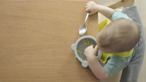 Top view high angle baby eating porridge holding spoon, helping fingers put food Stock Footage 206187879