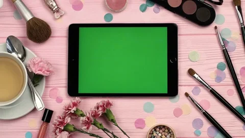 Top view of horizontal tablet with green screen on pink wooden table with make Stock Footage 73910864