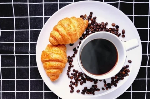 Top view of hot coffee cup with rising steam and fresh croissants on tablecloth Stock Footage 330586626
