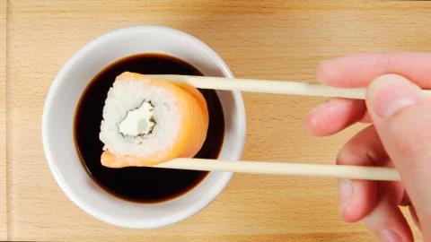 TOP VIEW: Human hand dips a sushi by chopsticks in a soy sauce cup Stock Photos