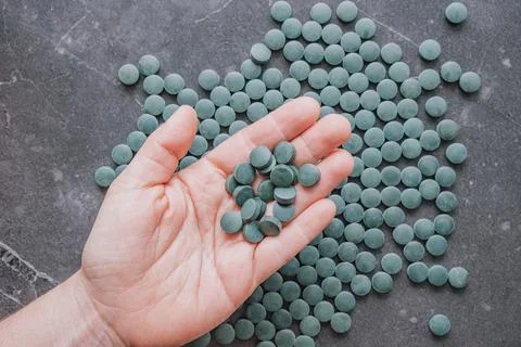 Top view of human hand holding group of green spirulina chlorella tablets o.. Stock Photos