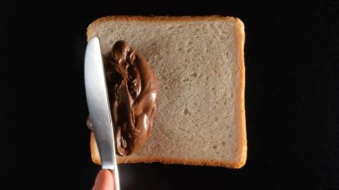 TOP VIEW: Human hand ready to spread a chocolate paste on a bread by a knife Stock Photos