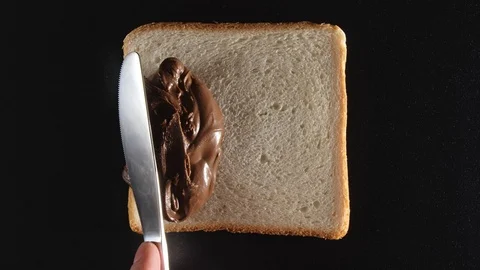 TOP VIEW: Human hand spreads a chocolate paste on a bread Vídeo Stock 70804850