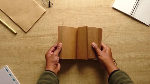 Top view of human hands opening and closing a notebook with blank brown pages Stock Footage 332193668