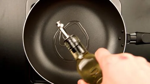 TOP VIEW: Human hands pouring olive oil on the frying pan Stock Photos