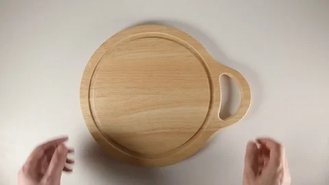 TOP VIEW: Human hands puts a round cutting board with handly on a white table Видео 74730214