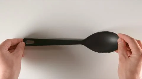 TOP VIEW: Human hands puts a black plastic spoon on a white table Stock Photos