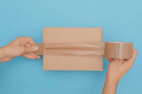 Top view of human hands wrap up a cardboard box with parcel tape, isolated on Stock Photos