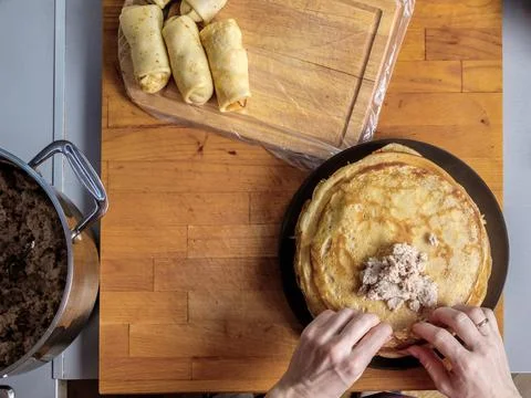 Top view on human hands wrapping meat filling in freshly baked pancake on a Stock Photos