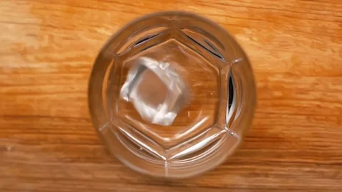 Top view of ice cubes falling into empty glass on wooden table, slow motion Stock Footage 132423983