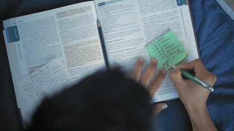 Top view, Indian Student taking notes from the Book on the Sticker,Lying on the Stock Footage 111072504